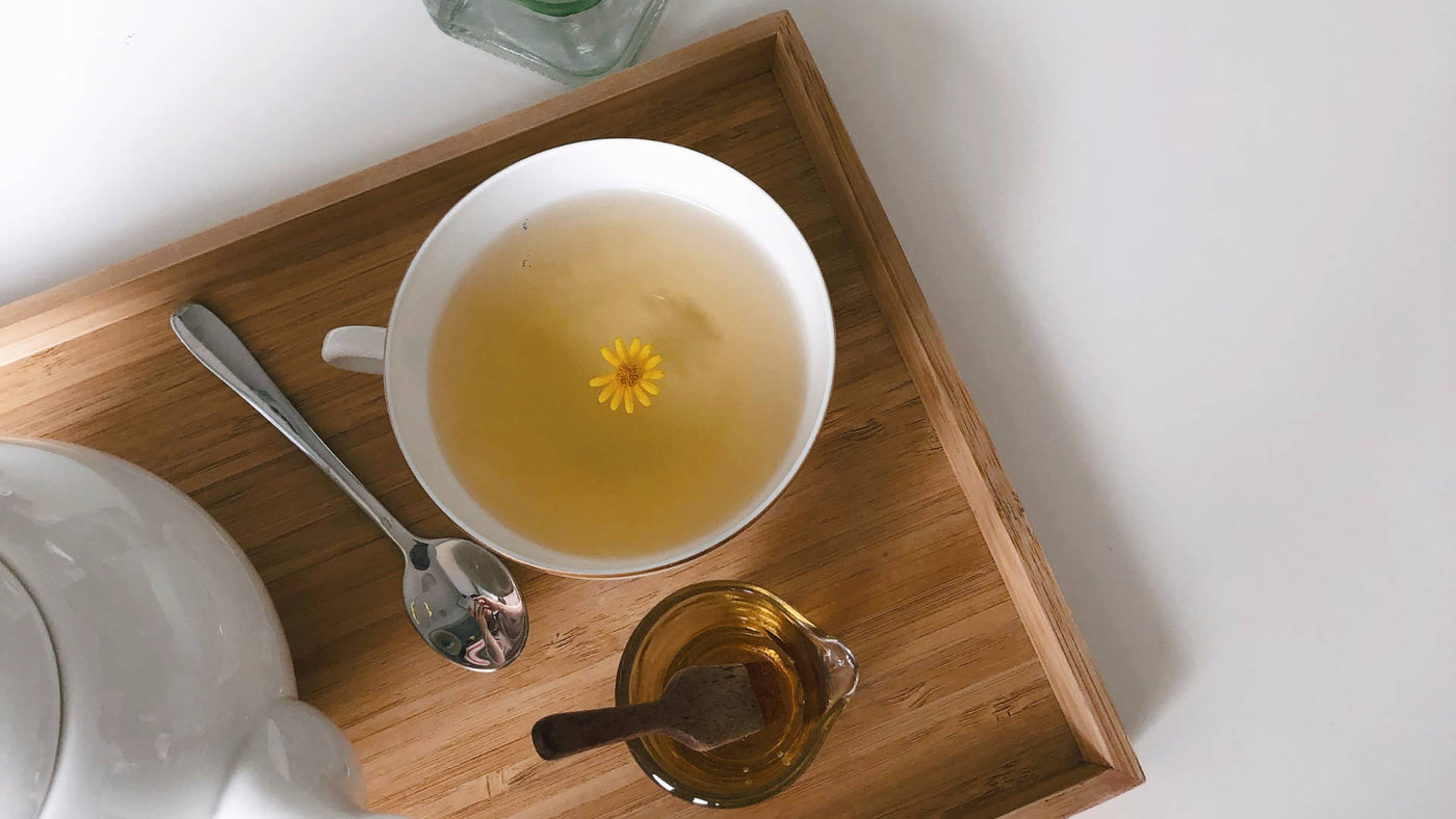 A tea in a teacup with teapot on a wooden serving tray.