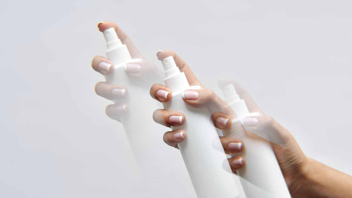 A hand with fine manicured french fingernails holding a white spray bottle on a white background.