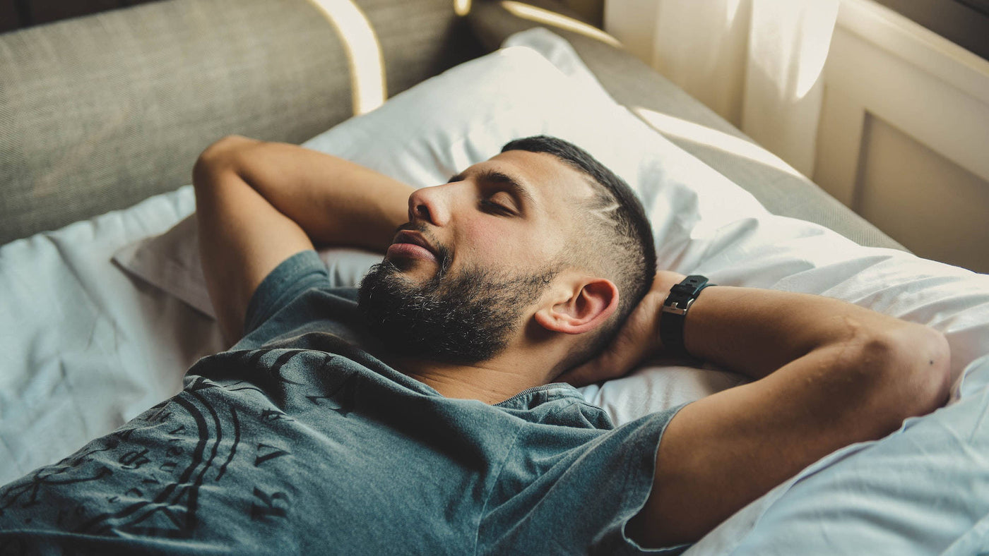 A man lying in bed with both of his hands behind his head.