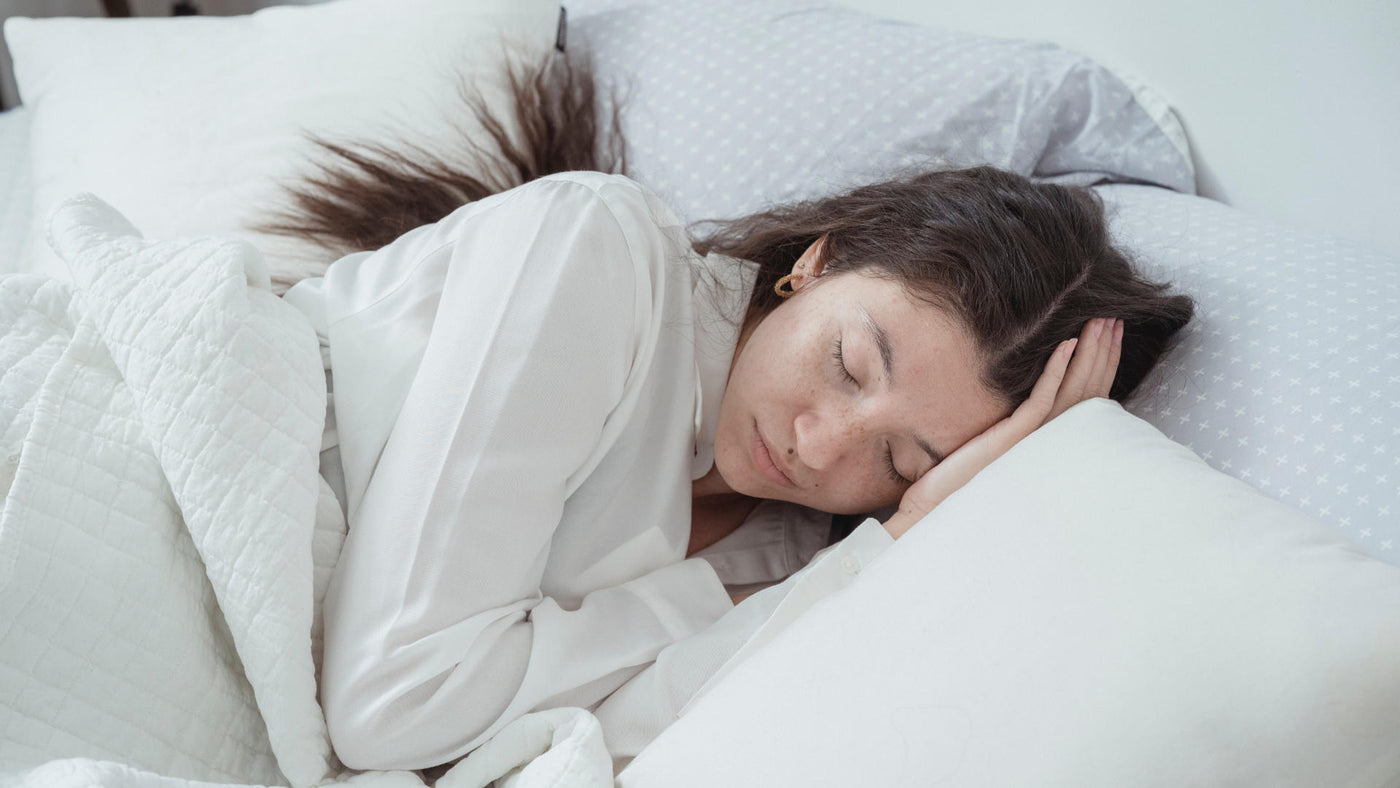 A woman sleeping deeply under white sheets on a bed.