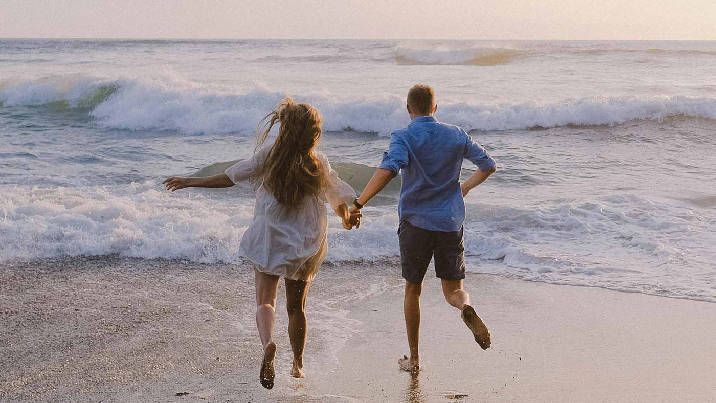 two people holding hands running on the beach